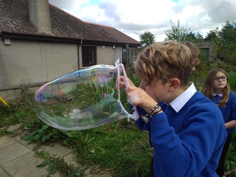 Image shows a child blowing giant bubbles