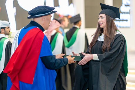 Graduate in robes and hat talking to a staff member