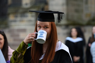 Someone in a cap and gown drinking out of a mug that reads 'Class of 2024'