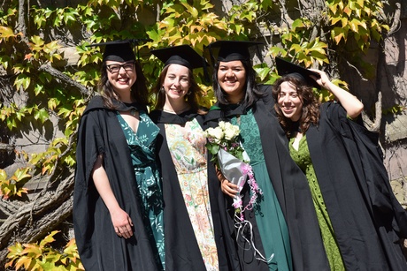 Four women smiling at the camera wearing caps and gowns