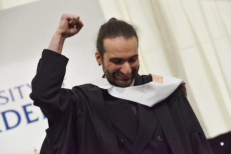 Man wearing graduation robes with his fist in the air smiling