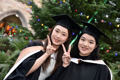 Two women doing peace signs with the Christmas tree behind them