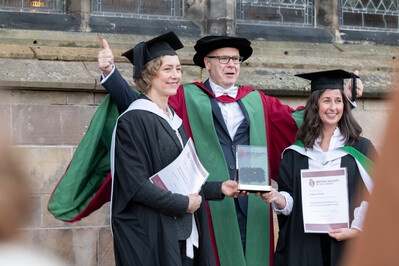 Three people in robes smiling for the camera