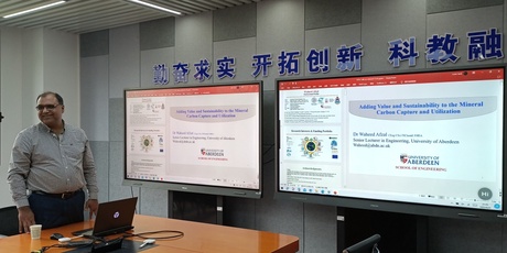 Waheed standing in front of two screens with his presentations