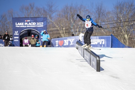 A photograph of skier Olivia Burke, grinding railings on the ski slope with a blue sky in the background