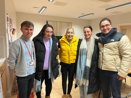 A photograph of 5 people standing alongside each other smiling