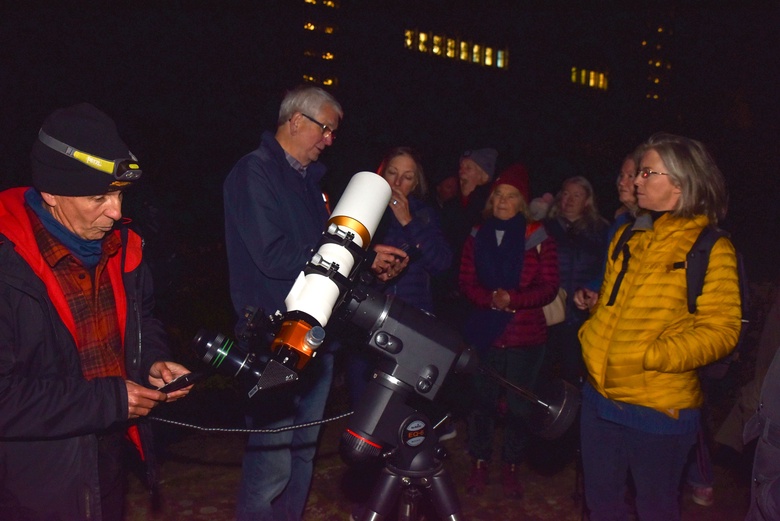 Visitors listen to an astronomer describing a telescope in the Rose Garden. It is dark and some visitors are wearing hats and gloves.