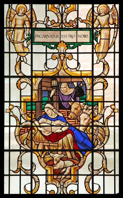 Stained glass depicting Mary with Jesus in a stable surrounded by farm animals with