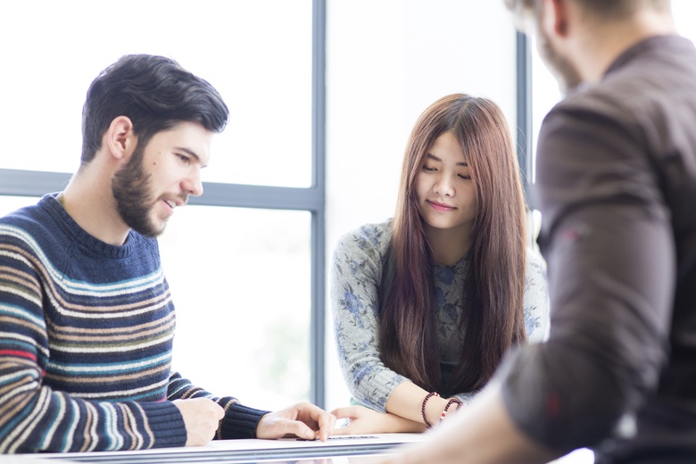 three students work on a group project around a table