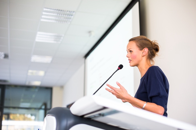 A woman stands at a podium delivering a presentation