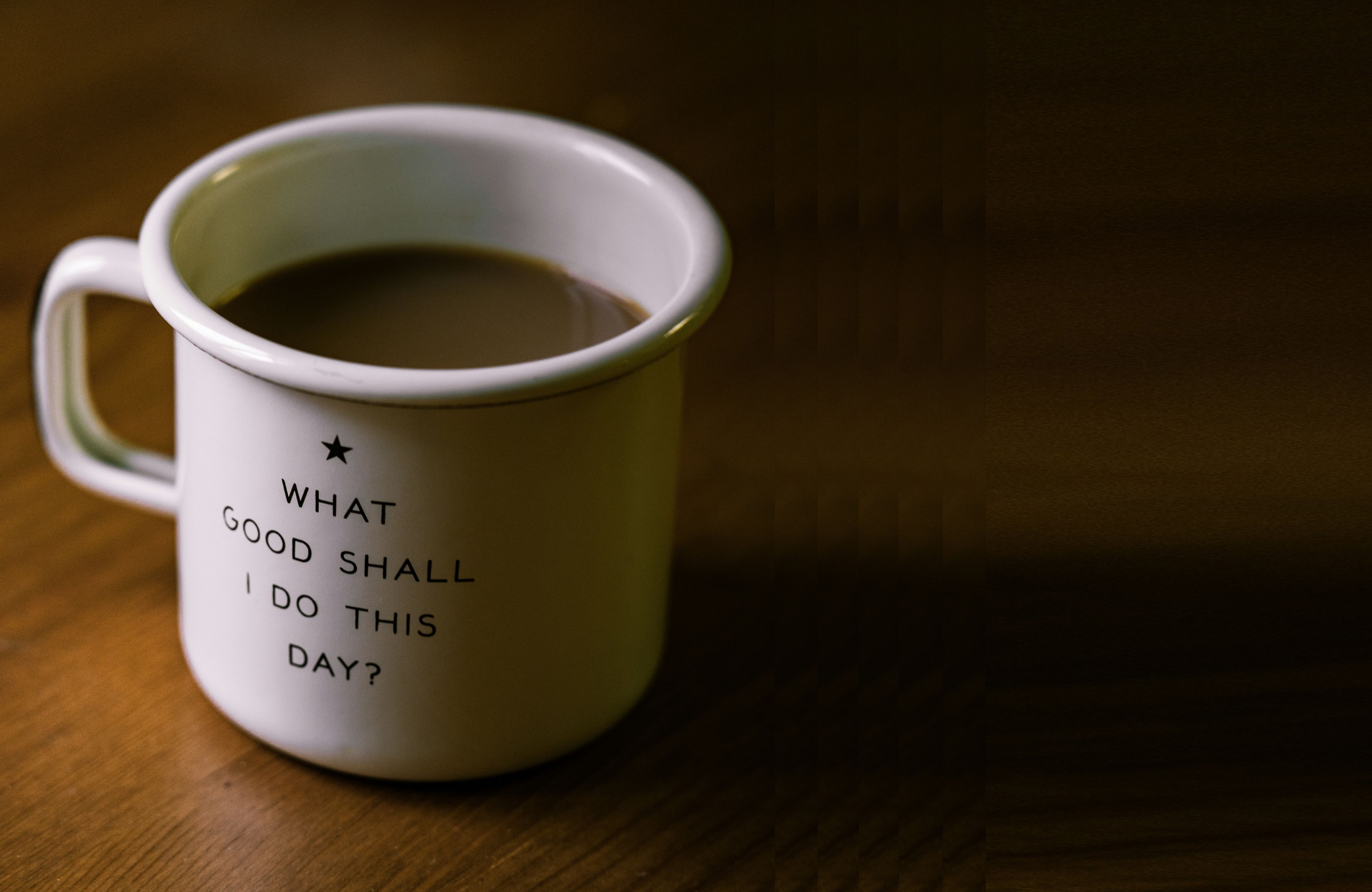 white and black ceramic cup filled with brown liquid on brown wooden sufface